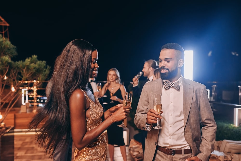 Beautiful young couple sugar daddy and sugar baby in formalwear holding champagne flutes and smiling while spending time on luxury party