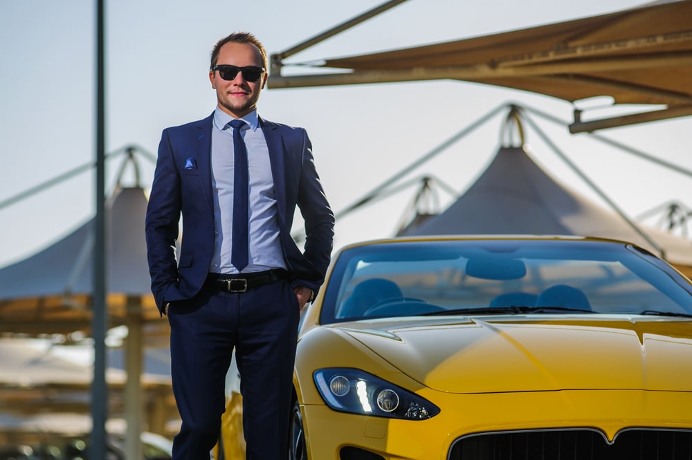 Successful millionaire stands next to yellow cabrio car.