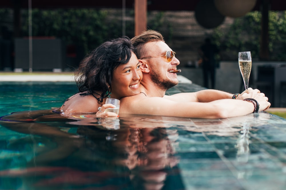 Luxuspärchen ruht sich im Pool mit Champagner und Zigarre aus