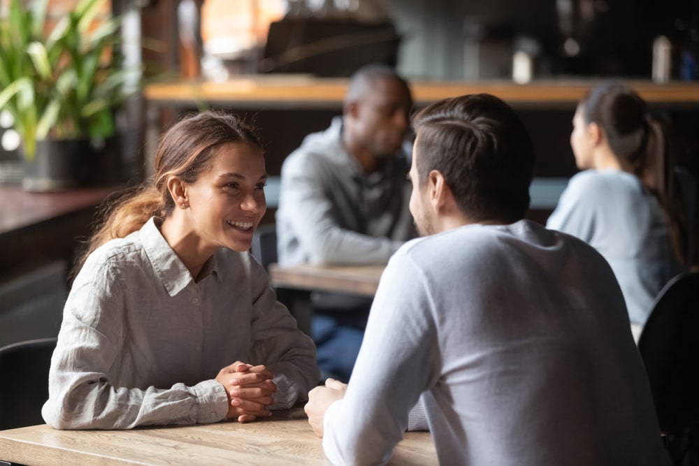 Happy sugar baby and her sugar daddy chatting sit at cafe table, smiling woman talking to man at date in restaurant