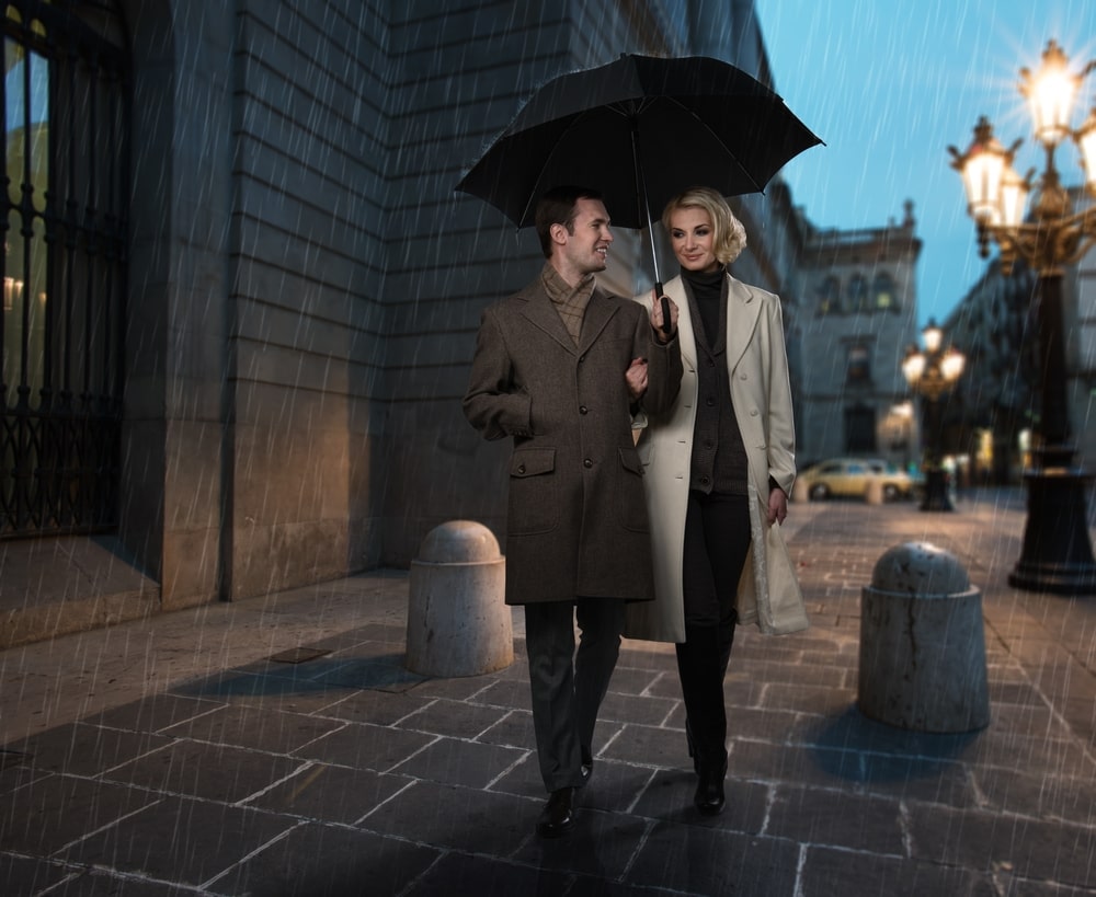 a rich couple on the street holding an umbrella and laughing, enjoying their relationship