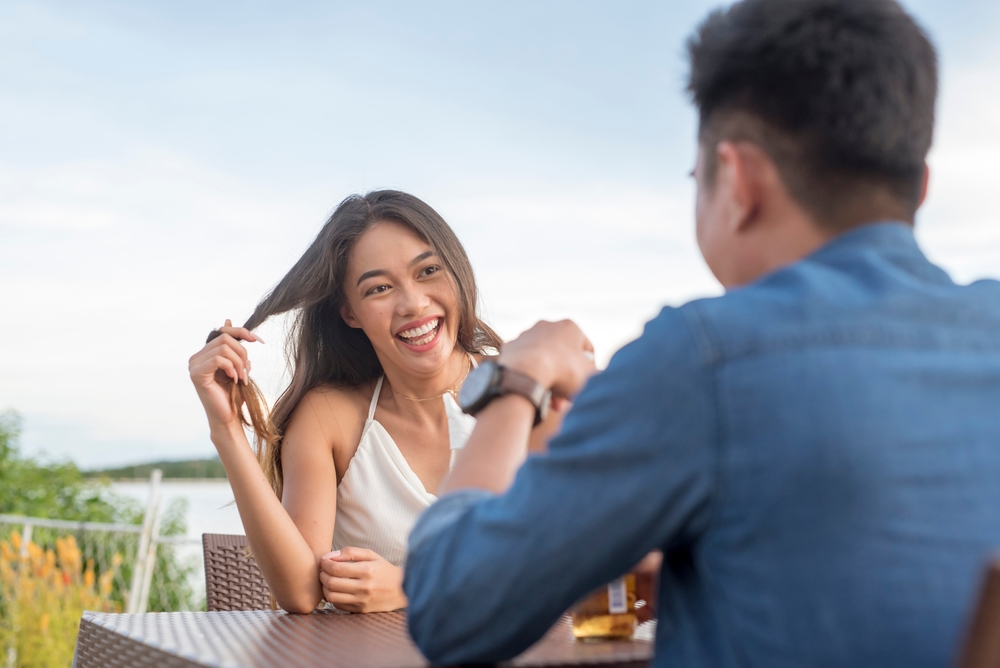 Laechelnde Frau spielt beim ersten Date mit ihren Haaren und zeigt Interesse